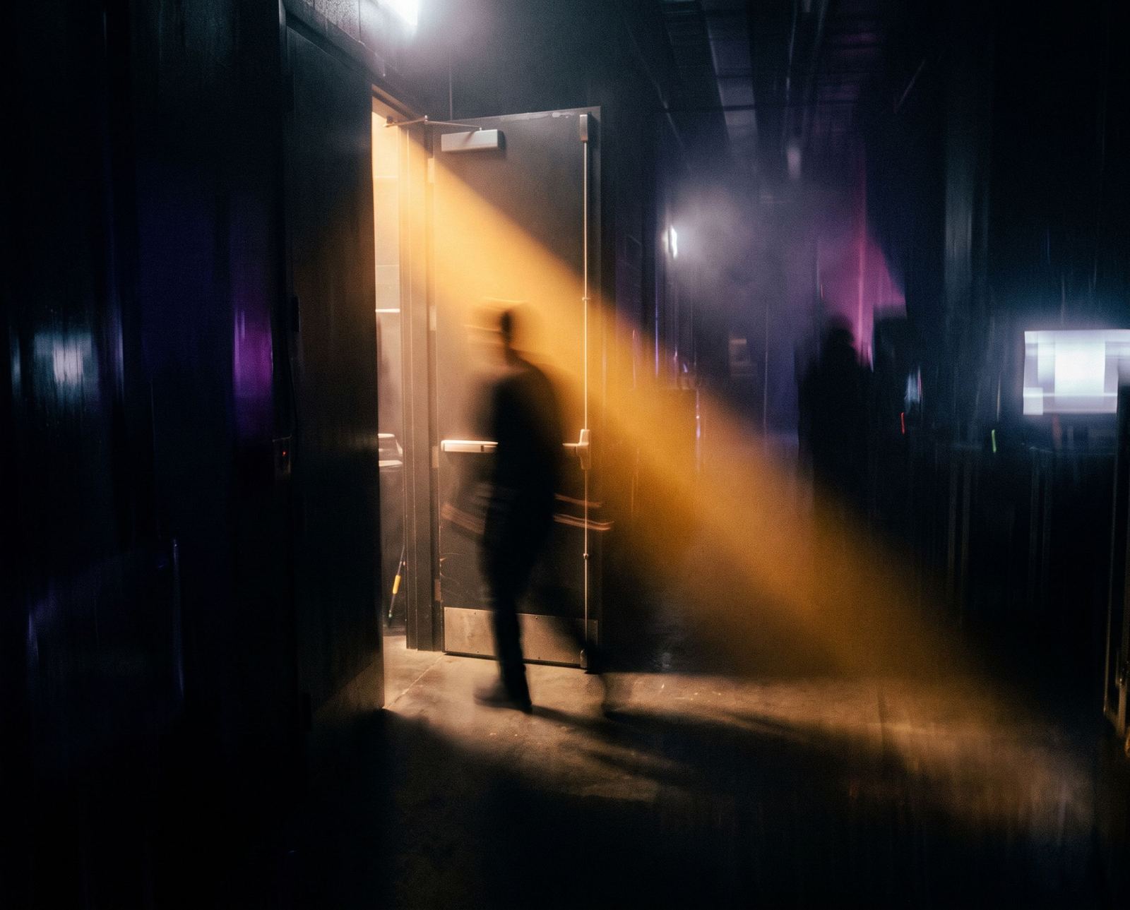 Backstage-Gang im Dunst, ein Amber-Lichtstrahl fällt durch die Tür, eine Silhouette geht hindurch