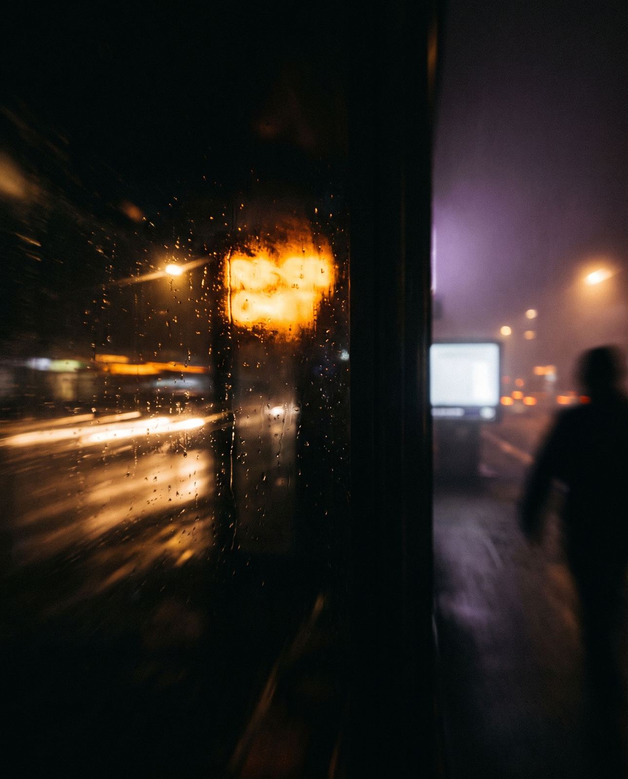 Nachts durch eine verregnete Scheibe: Lichtschweife der Stadt, ein Amber-Neon, eine Silhouette